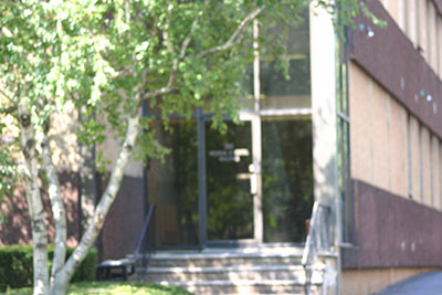 The image shows a building entrance with a glass door and a metal railing.