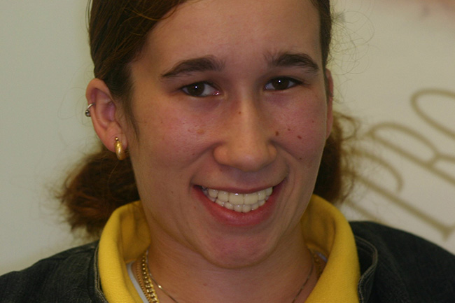 The image shows a person with a smile, wearing glasses and a yellow top, against a white background.
