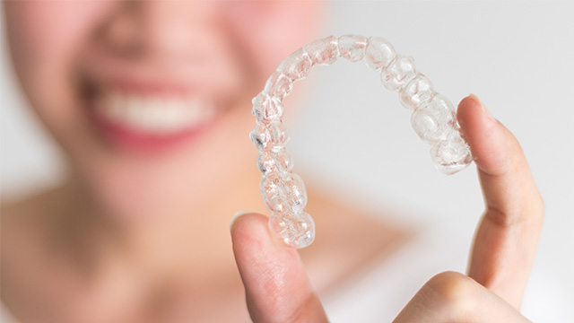 An image featuring a person holding a transparent, crystalline dental retainer with their hand.