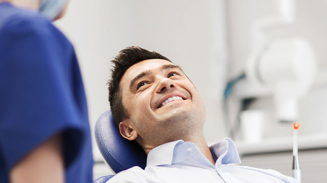 A man is seated in a dental chair with a smiling expression, while a dentist stands behind him, both in a dental office setting.