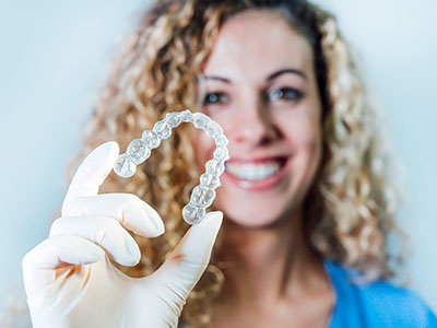 A person is holding a clear dental retainer, smiling and showcasing it.