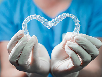 An image featuring a person in a blue uniform, holding up a transparent dental retainer with a heart shape, symbolizing love or care for dental health.