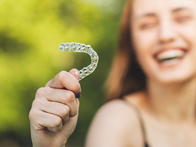 An image of a person holding a transparent dental retainer with the teeth inside, smiling towards the camera.