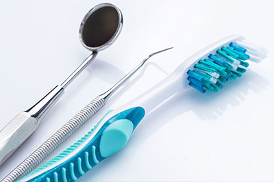 The image shows a collection of dental instruments, including a toothbrush with blue bristles, placed on a white background alongside a pair of scissors and a metal spoon-like tool.