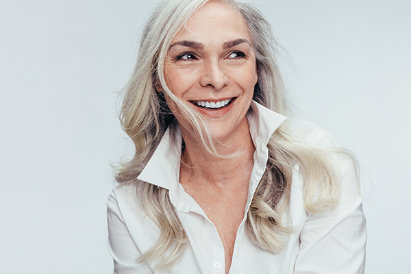 A woman with short hair, wearing a white blouse, smiling and looking directly at the camera.