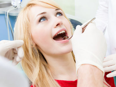 A woman in a dentist s chair receiving dental care, with a dental professional examining her teeth.