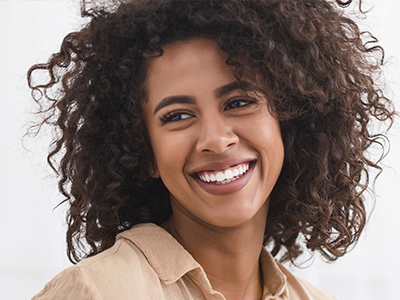 The image shows a woman with curly hair, smiling and looking directly at the camera.